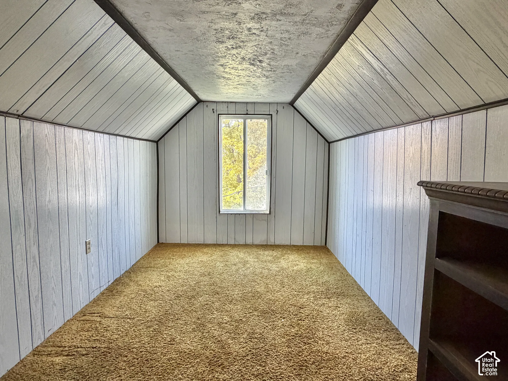 Vaulted ceilings featuring vertical wood-panel wall treatments, wall-to-wall carpeting, and a single-pane sliding window