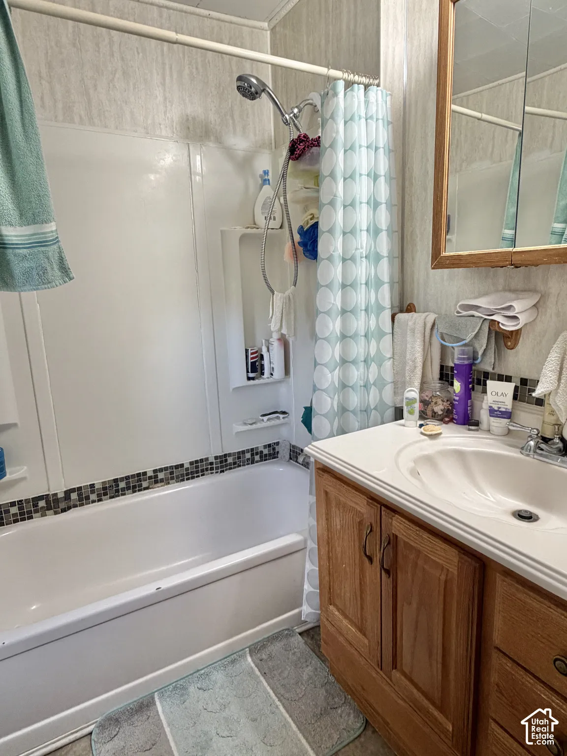Bathroom featuring a wood vanity with a molded basin, wall-mounted medicine cabinet, bathtub with a tiled accent border, and adjustable handheld shower head