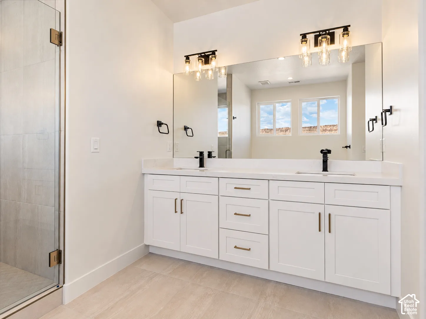 Double vanity featuring shaker-style cabinetry, a solid surface countertop, matte black fixtures, and dual integrated sinks beneath large-scale vanity lighting