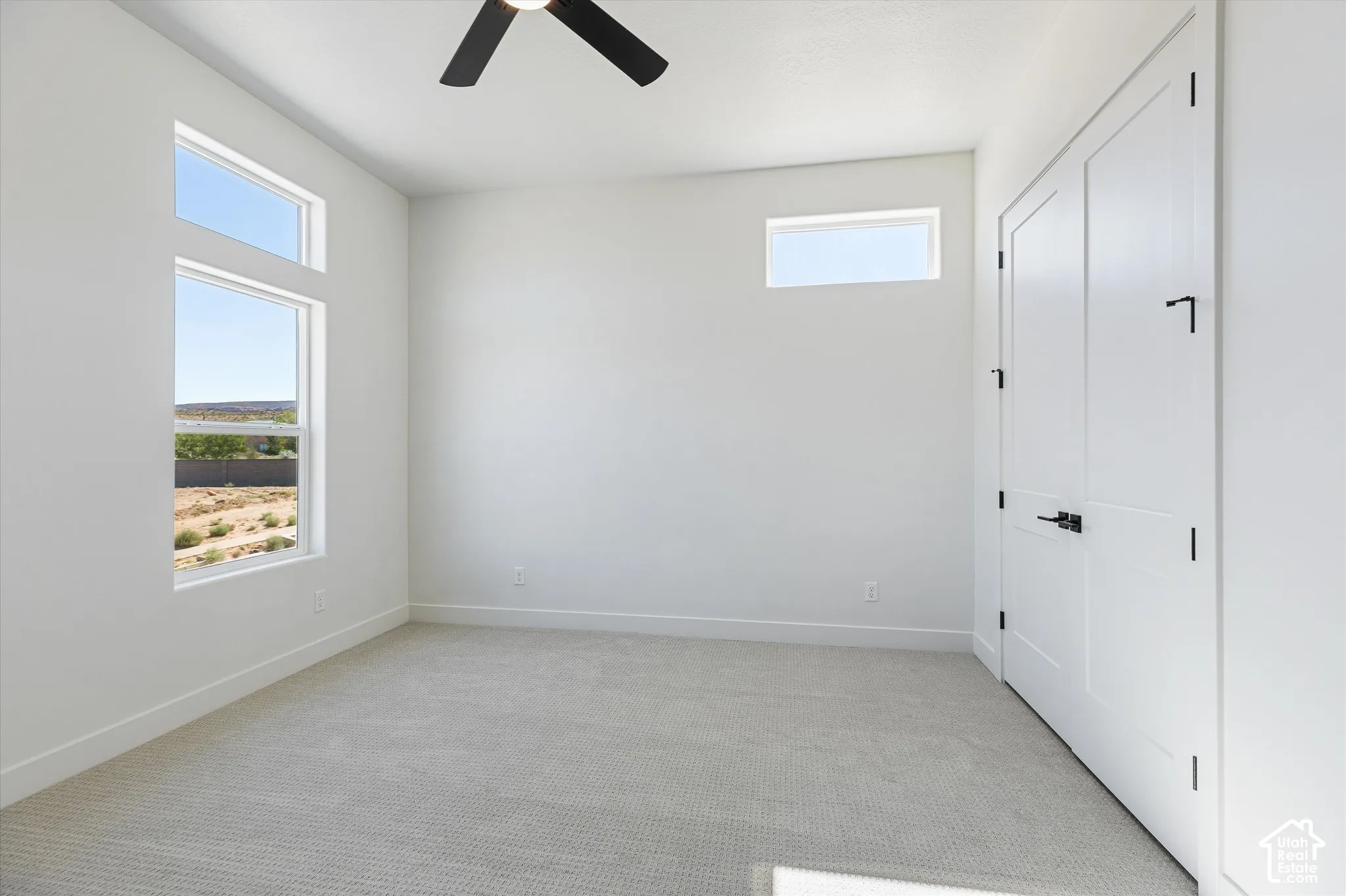 Neutral-toned wall-to-wall carpeting, high-reaching ceilings, clerestory windows, matte black ceiling fan, and double-panel doors with matte black hardware