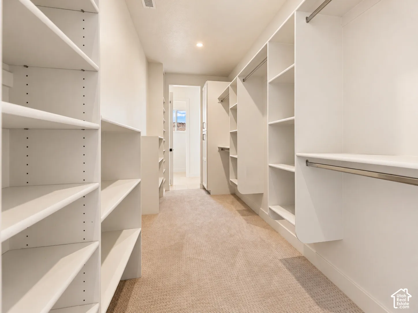 Customized walk-in closet featuring white built-in shelving, multiple hanging rods, and neutral carpeting