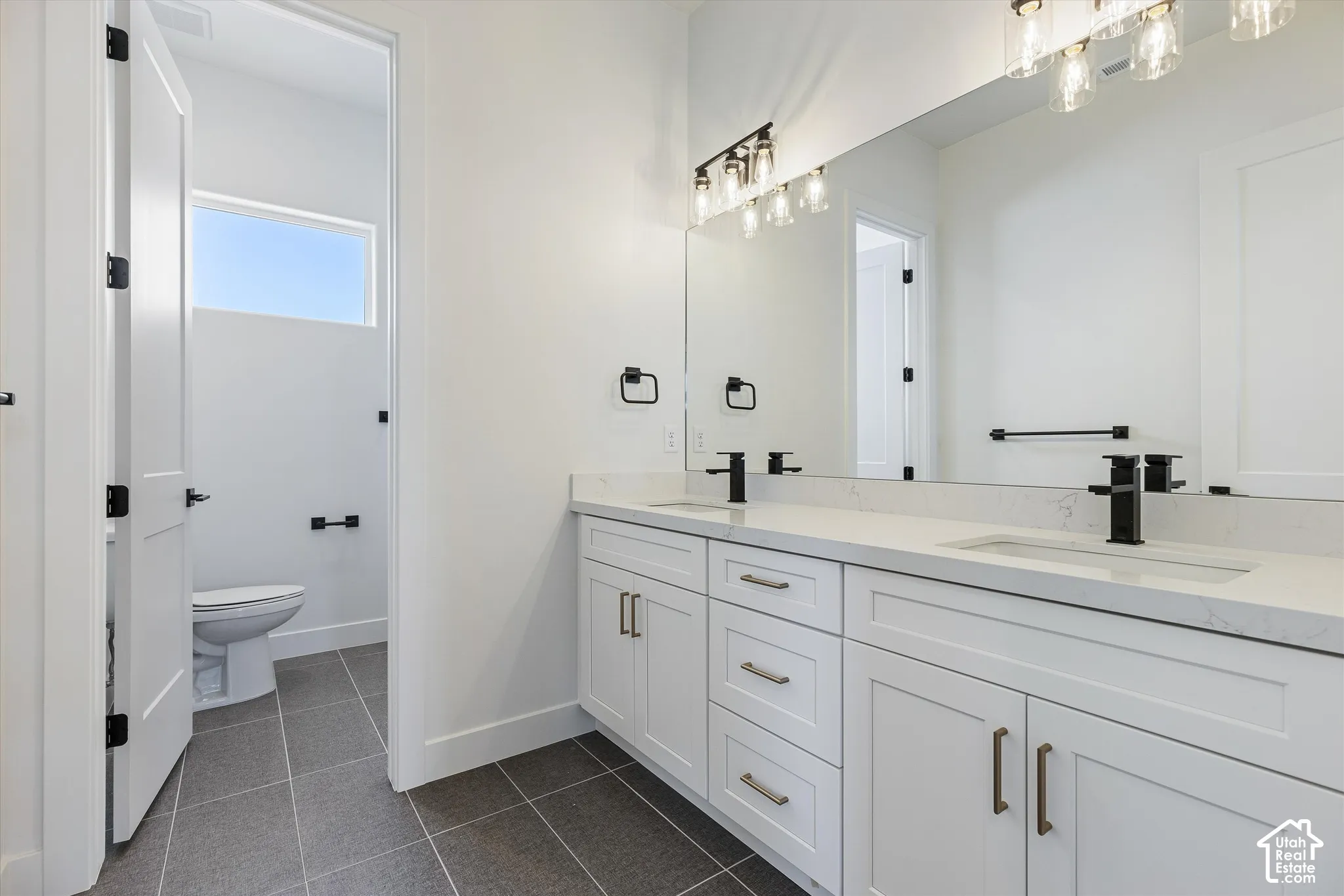 Dual-sink vanity with white cabinetry, stone-finish countertops, matte black plumbing fixtures, and large-format tile flooring