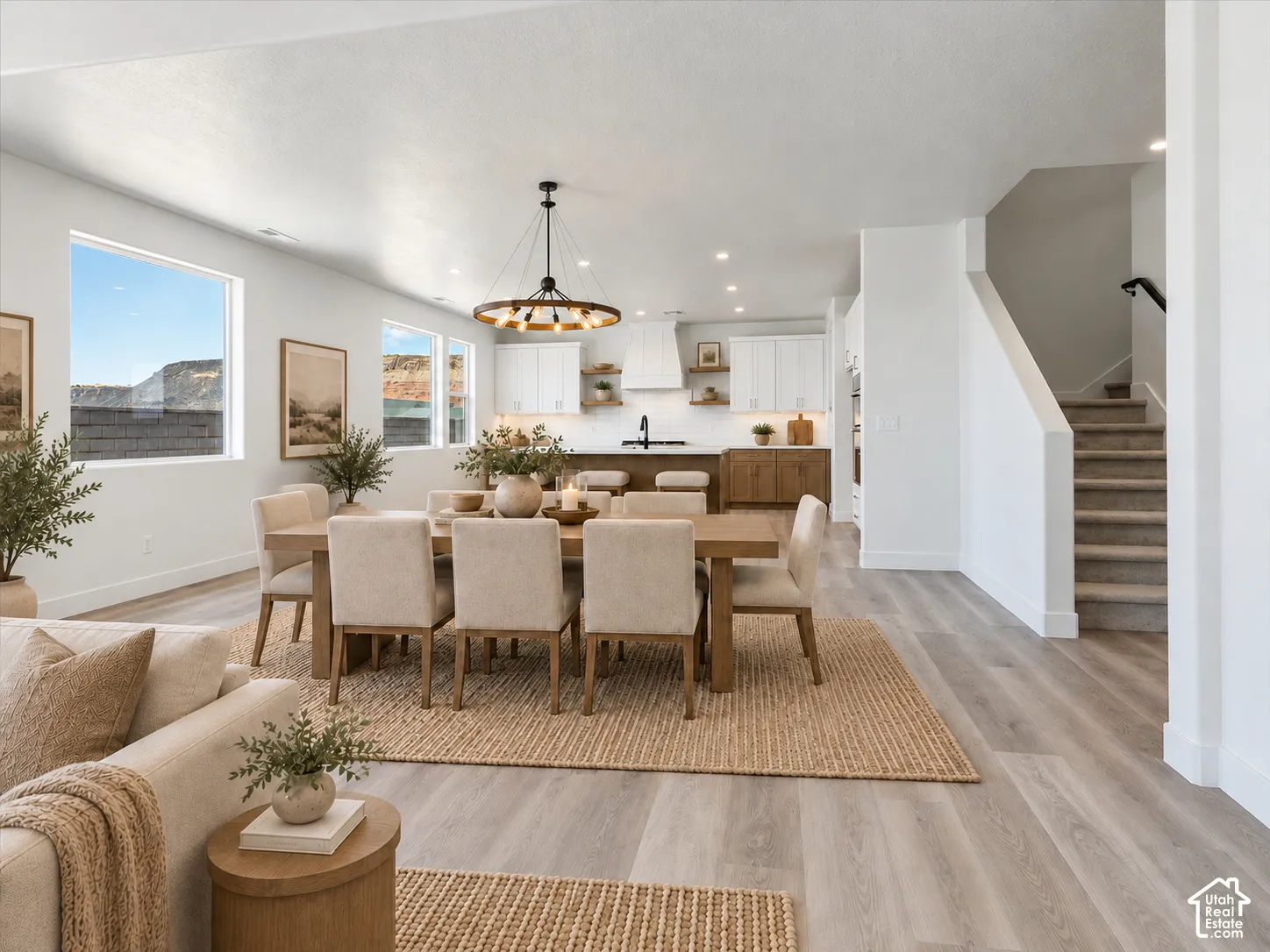 Open-concept kitchen and dining area featuring wood-finish flooring, a large kitchen island, white shaker-style cabinetry, and a wagon-wheel chandelier