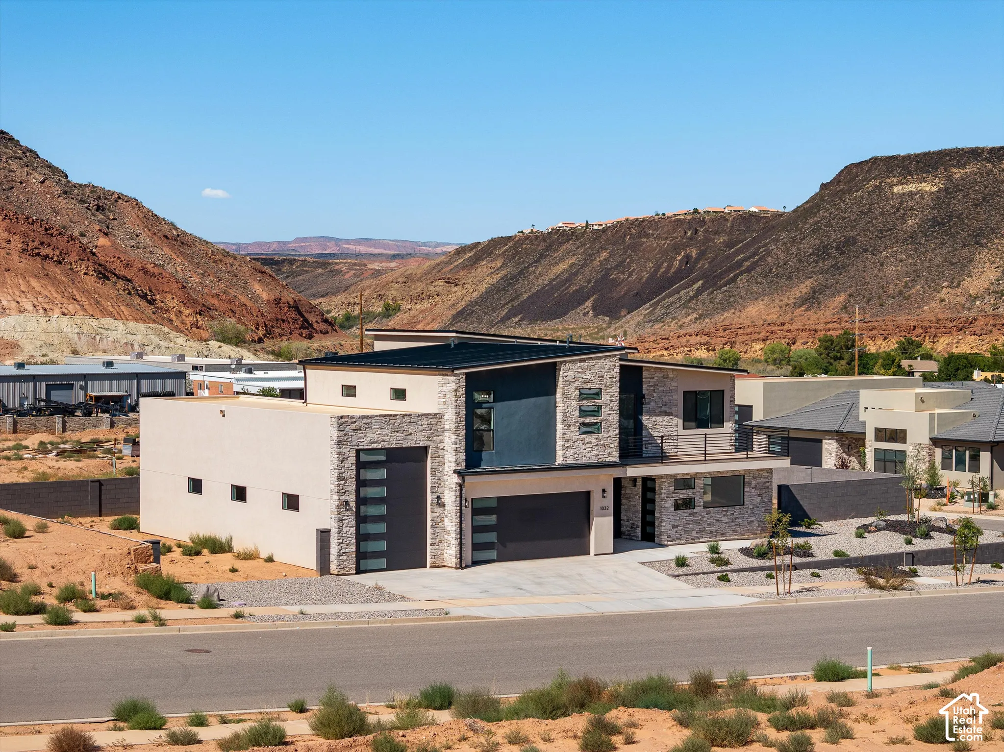 Contemporary residence featuring a stone veneer exterior, flat roofline, attached multi-car garage, second-story balcony, and natural desert backdrop