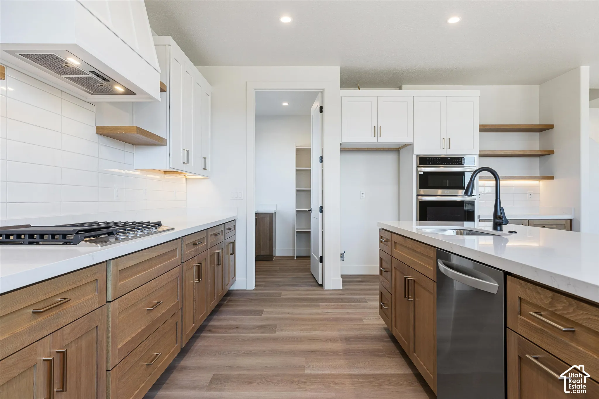 Kitchen featuring a center island, quartz countertops, two-tone cabinetry with wood-finish lowers and white uppers, subway tile backsplash, and built-in stainless steel double ovens