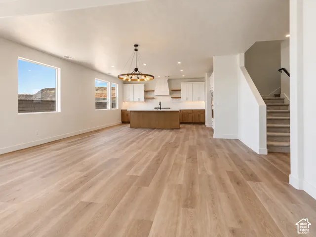 Open-concept interior featuring light wood-finish flooring, a central kitchen island with contrasting cabinetry, a large circular chandelier, and natural mountain scenery visible through expansive windows