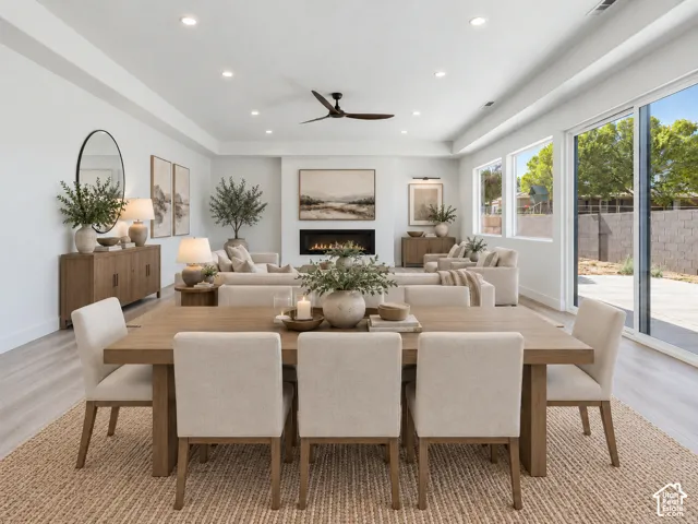 Open-concept living space featuring a linear gas fireplace with a recessed mantel, wood-finish flooring, tray ceiling with recessed lighting, and expansive sliding glass doors