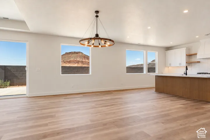 Open concept interior featuring light wood-finish flooring, a wrought-iron wagon wheel chandelier, recessed lighting, white cabinetry with a wood-accented kitchen island, and multiple windows showcasing a mountain backdrop