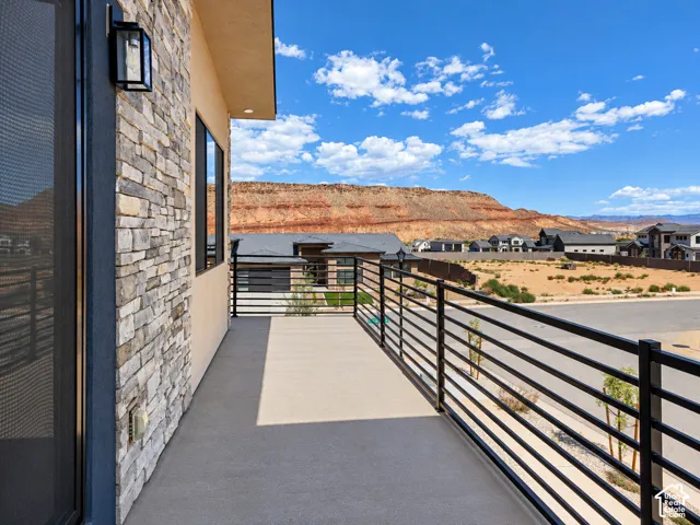 Balcony featuring a stacked stone exterior wall, matte black metal railing, concrete flooring, and an exterior wall-mounted light fixture, with a backdrop of desert mesas