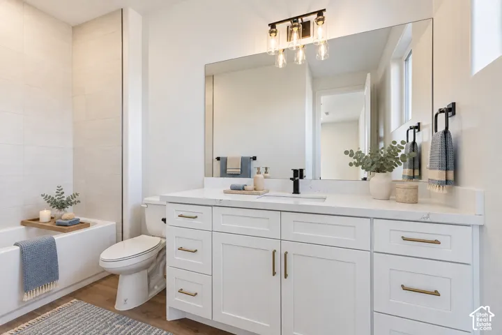 Bathroom featuring a white shaker-style vanity with stone-finish countertop, matte black faucet, wall-to-wall mirror, and a bathtub with tiled surround
