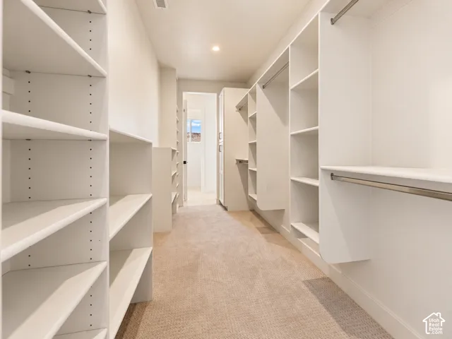Customized walk-in closet featuring white built-in shelving, multiple hanging rods, and neutral carpeting