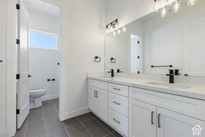 Dual-sink vanity with white cabinetry, stone-finish countertops, matte black plumbing fixtures, and large-format tile flooring