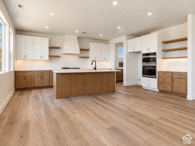 Kitchen featuring two-tone cabinetry, wood-finish flooring, quartz countertops, a custom hood range, and built-in double wall ovens