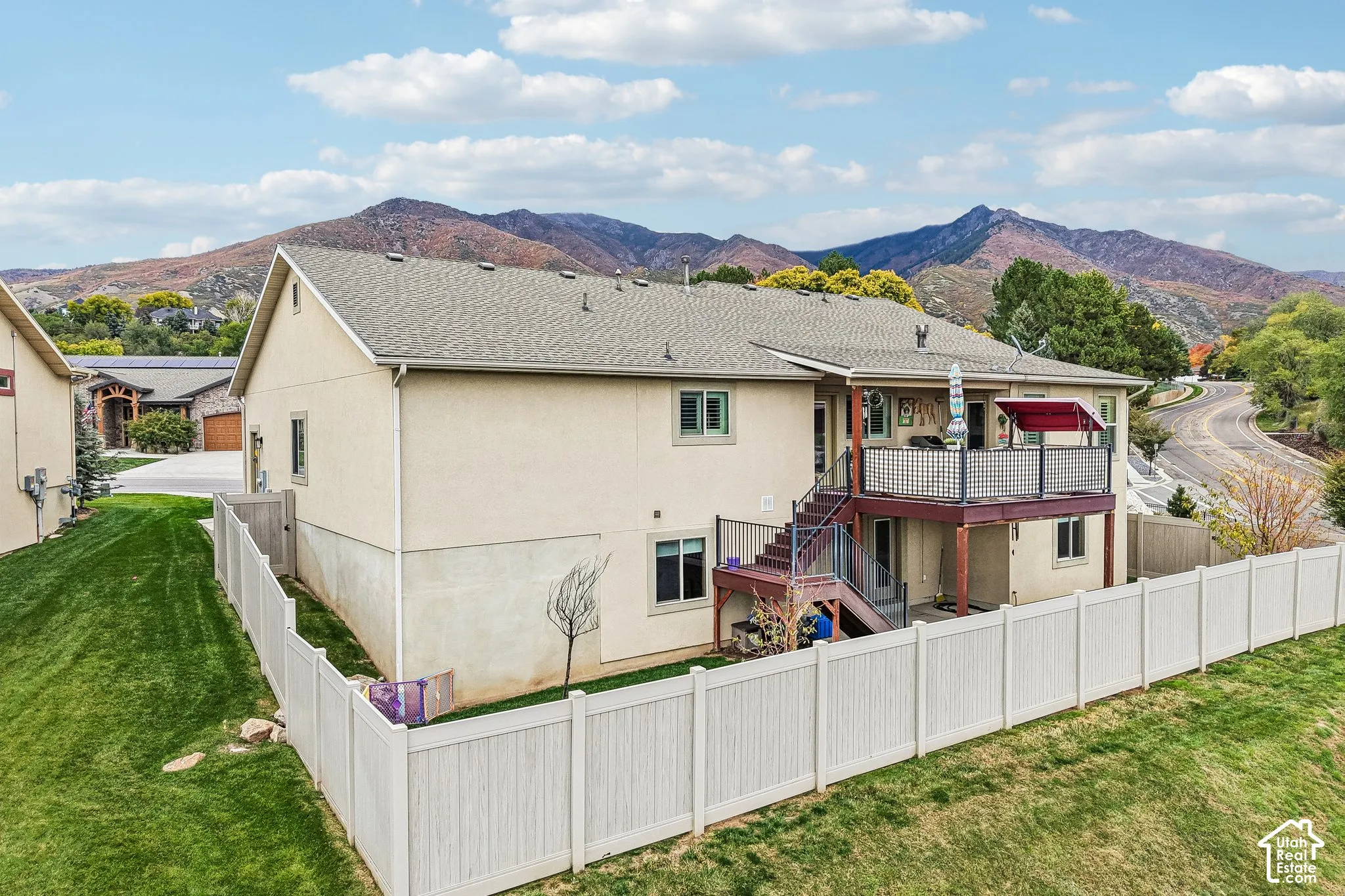 Stucco exterior with an elevated deck featuring metal railing and stairs, mountain backdrop, and enclosed backyard with vinyl fencing