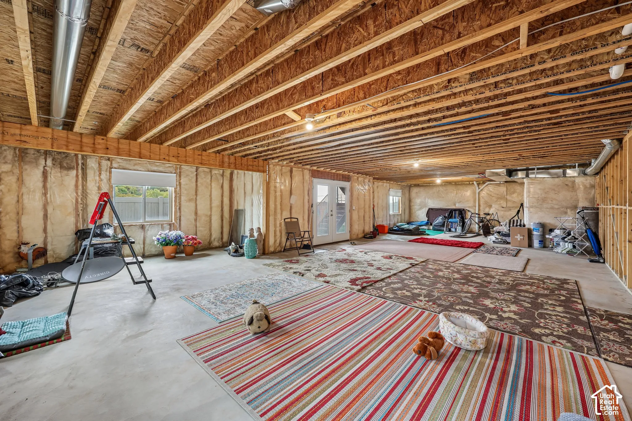 Unfinished lower level featuring exposed wood-joist ceilings, concrete flooring, insulated wall panels, and direct-access double doors