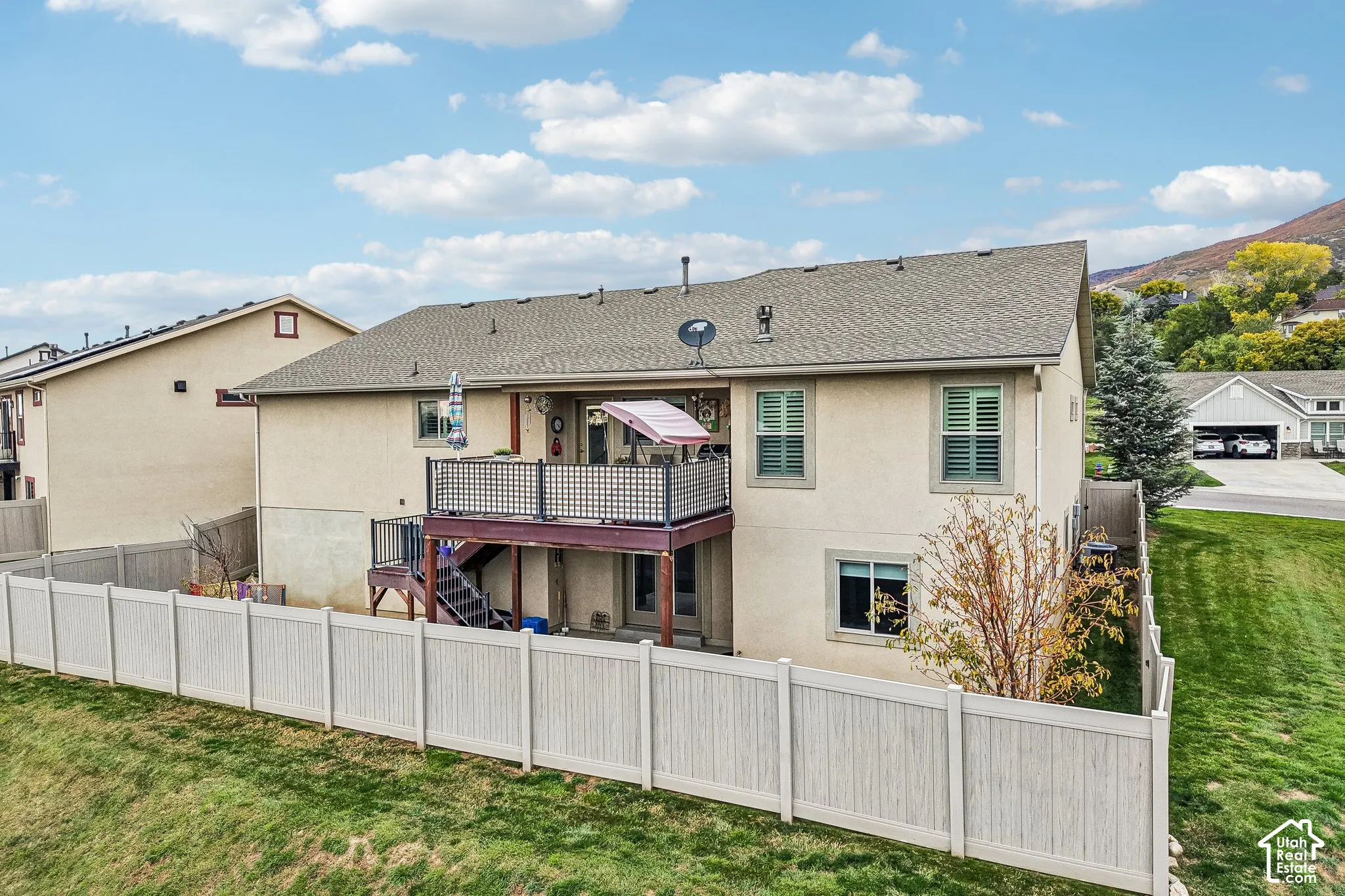 Two-story stucco exterior with an elevated deck, staircase, vinyl privacy fencing, and mountain backdrop