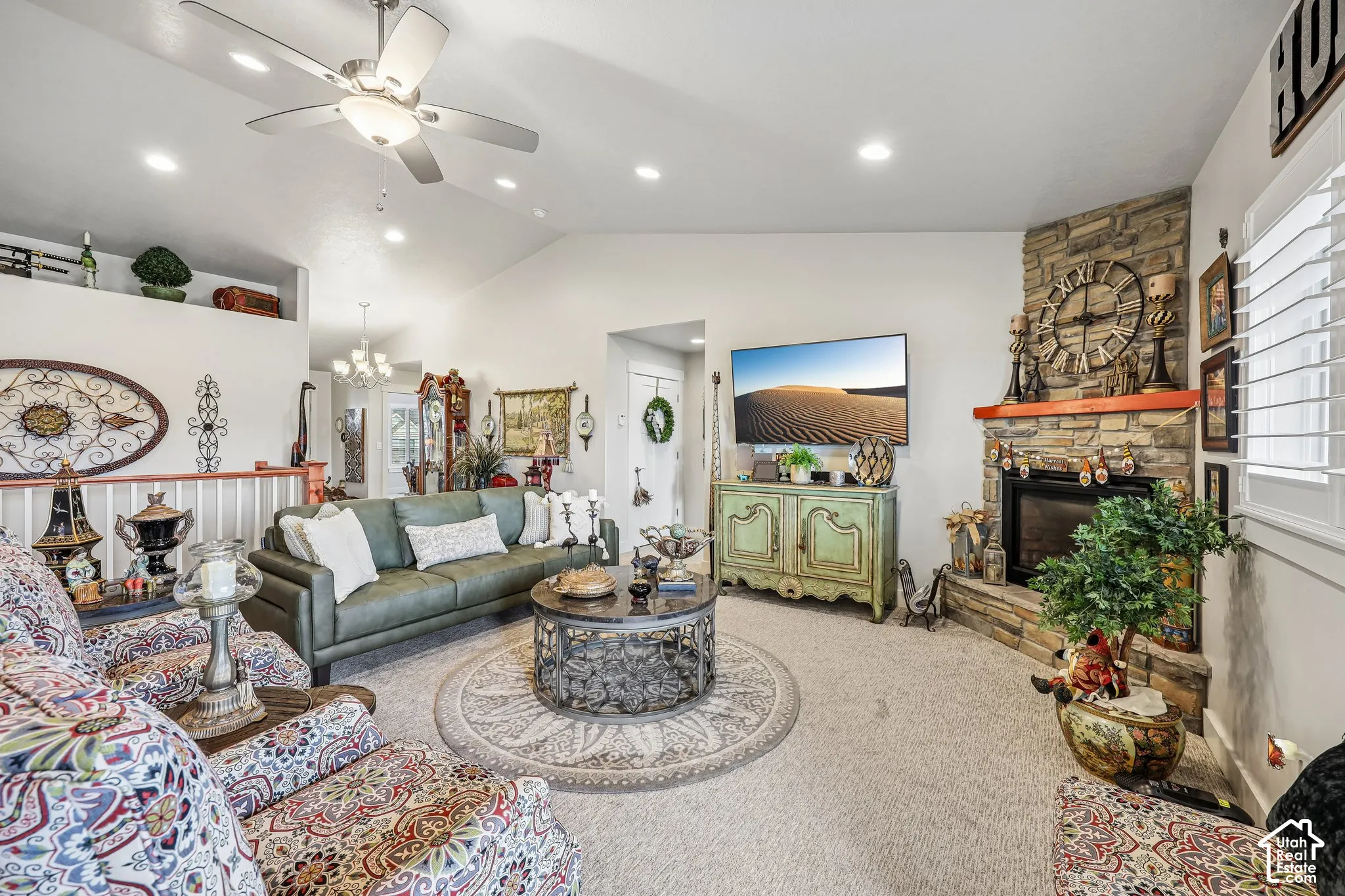 Vaulted ceilings with recessed lighting, stone-faced corner fireplace, wooden mantel, ceiling fan, and plantation shutters