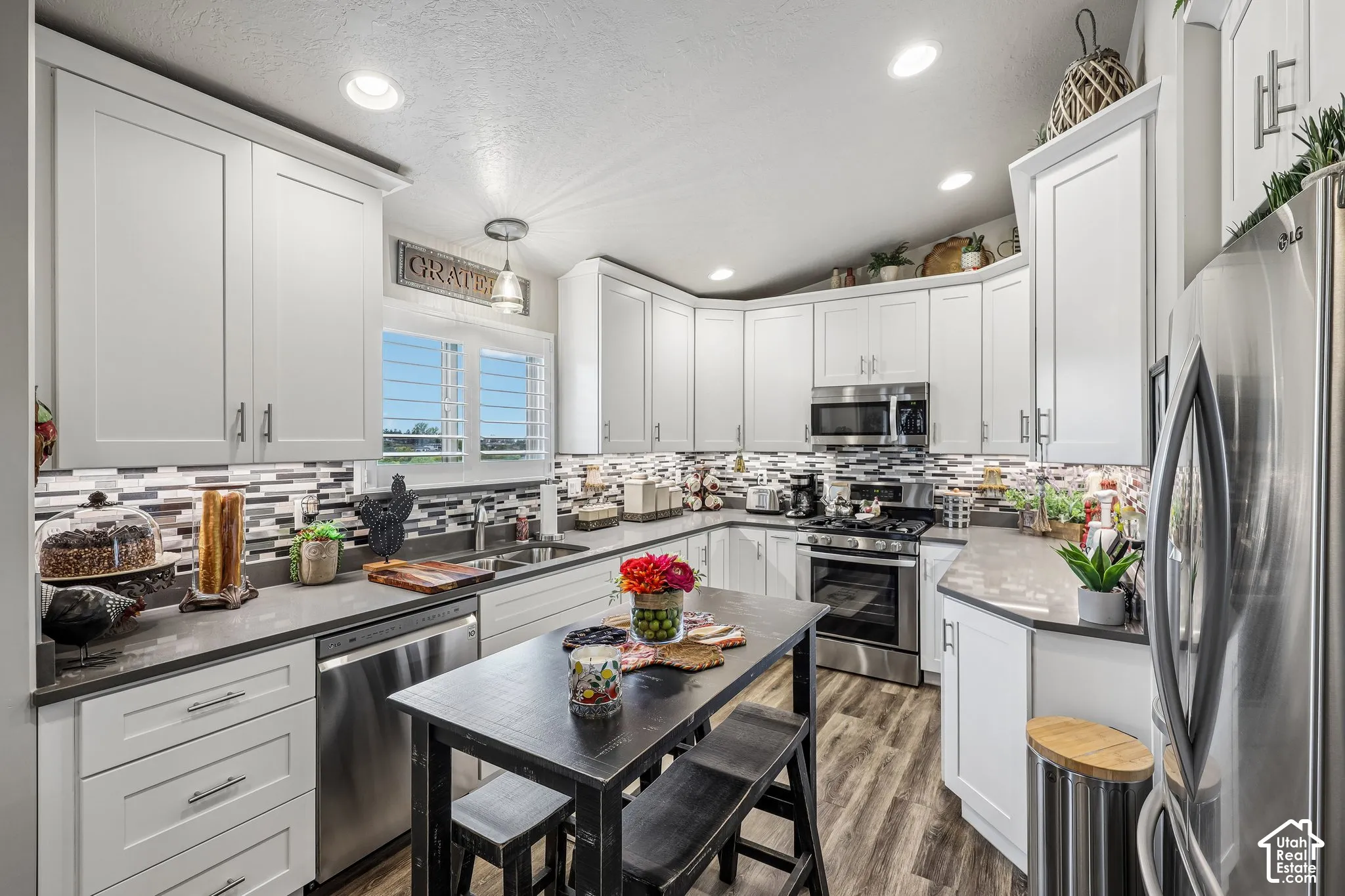 Kitchen featuring white shaker-style cabinetry, solid-surface countertops, a multicolored mosaic tile backsplash, stainless steel appliances, and wood-finish flooring