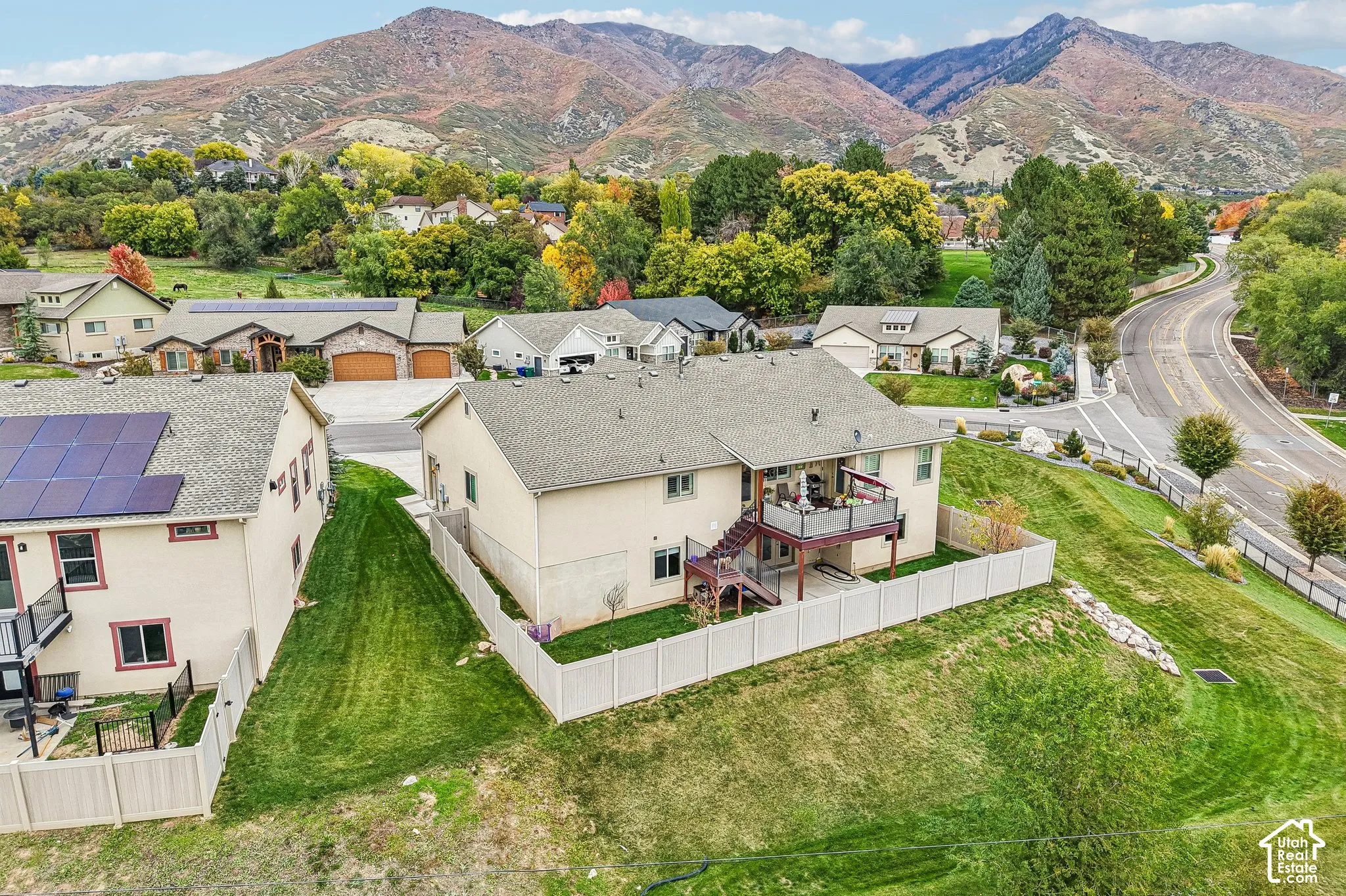 Aerial perspective of a multi-level residence featuring a fenced backyard, an elevated deck, and a mountain backdrop