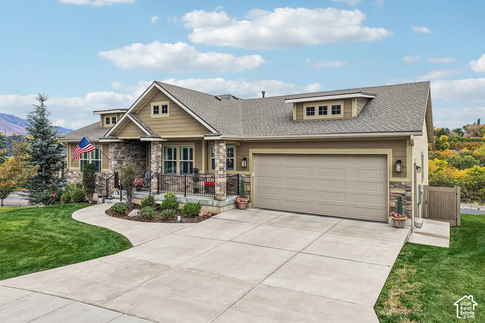Exterior facade featuring horizontal siding and stone veneer accents, covered front porch with iron railing, gabled roofline with dormers, and an attached two-car garage