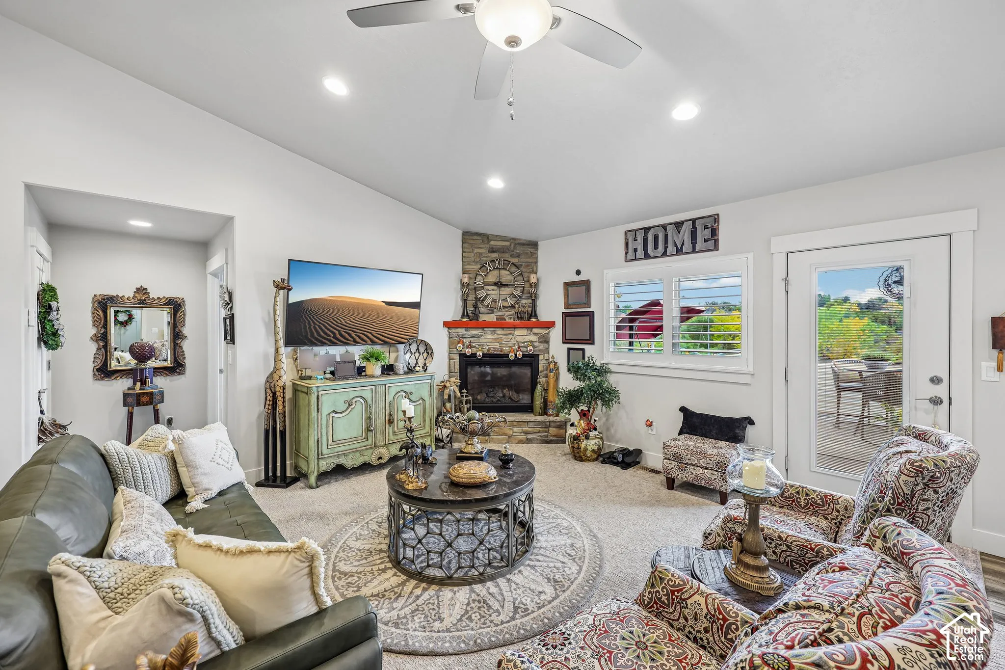 Vaulted ceiling featuring a central light fixture and ceiling fan, corner fireplace with stone veneer surround, recessed lighting, and white plantation shutters