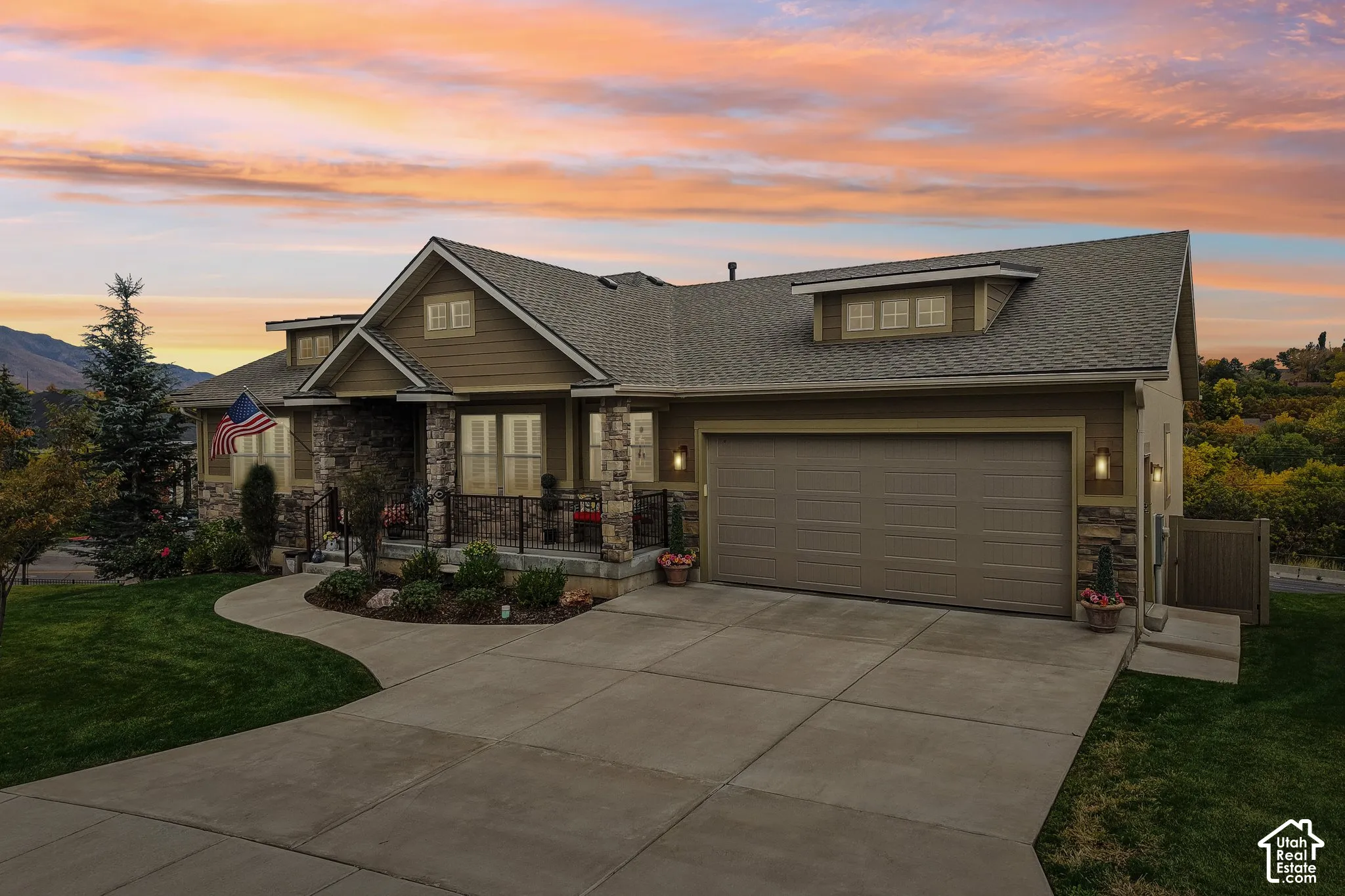 Exterior featuring horizontal siding with stone veneer accents, multi-gabled roofline, concrete driveway, and covered porch with metal railing