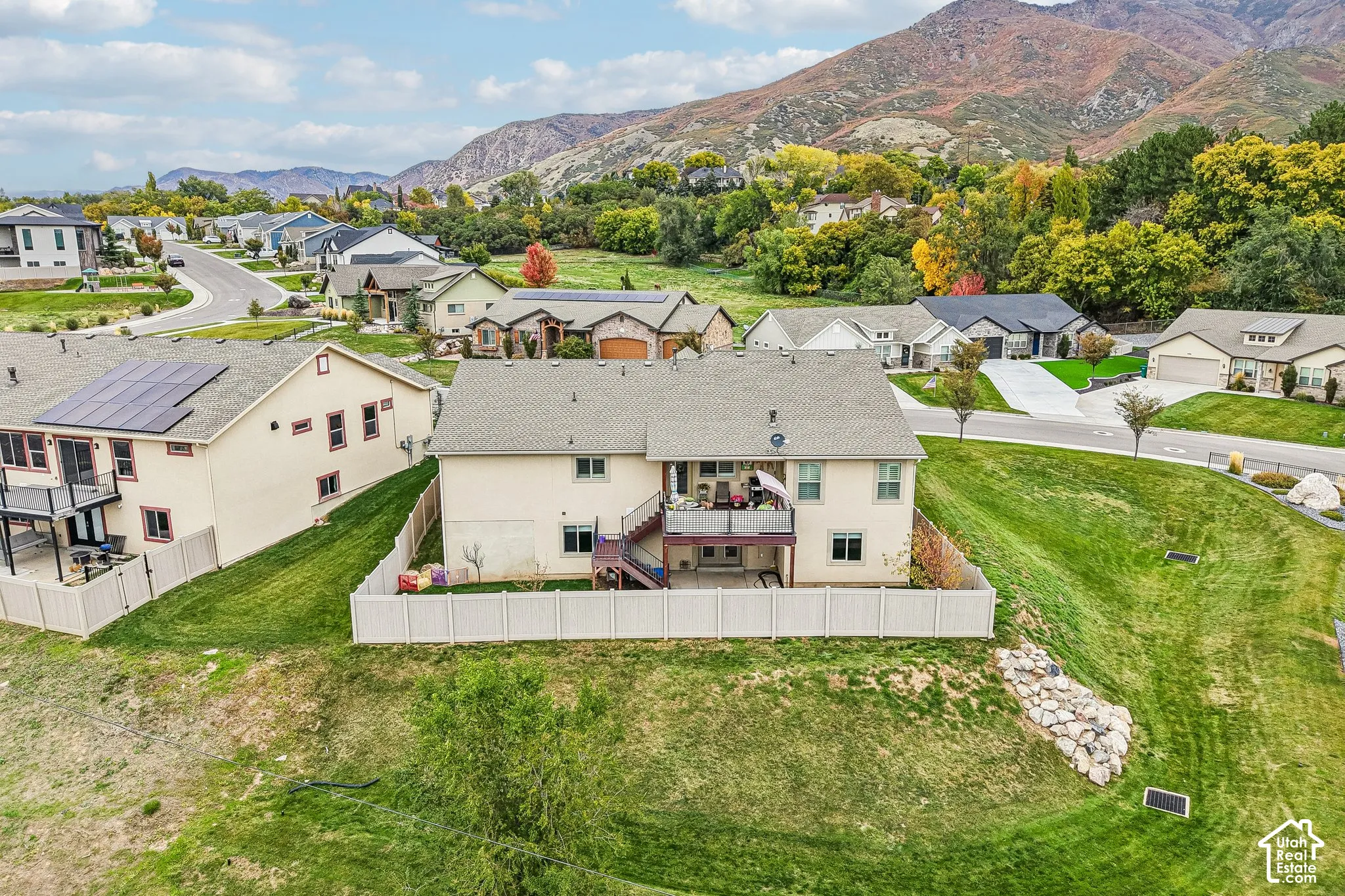 Two-story residence featuring an elevated deck with stairs, a paved patio, a fenced backyard, and mountain backdrop