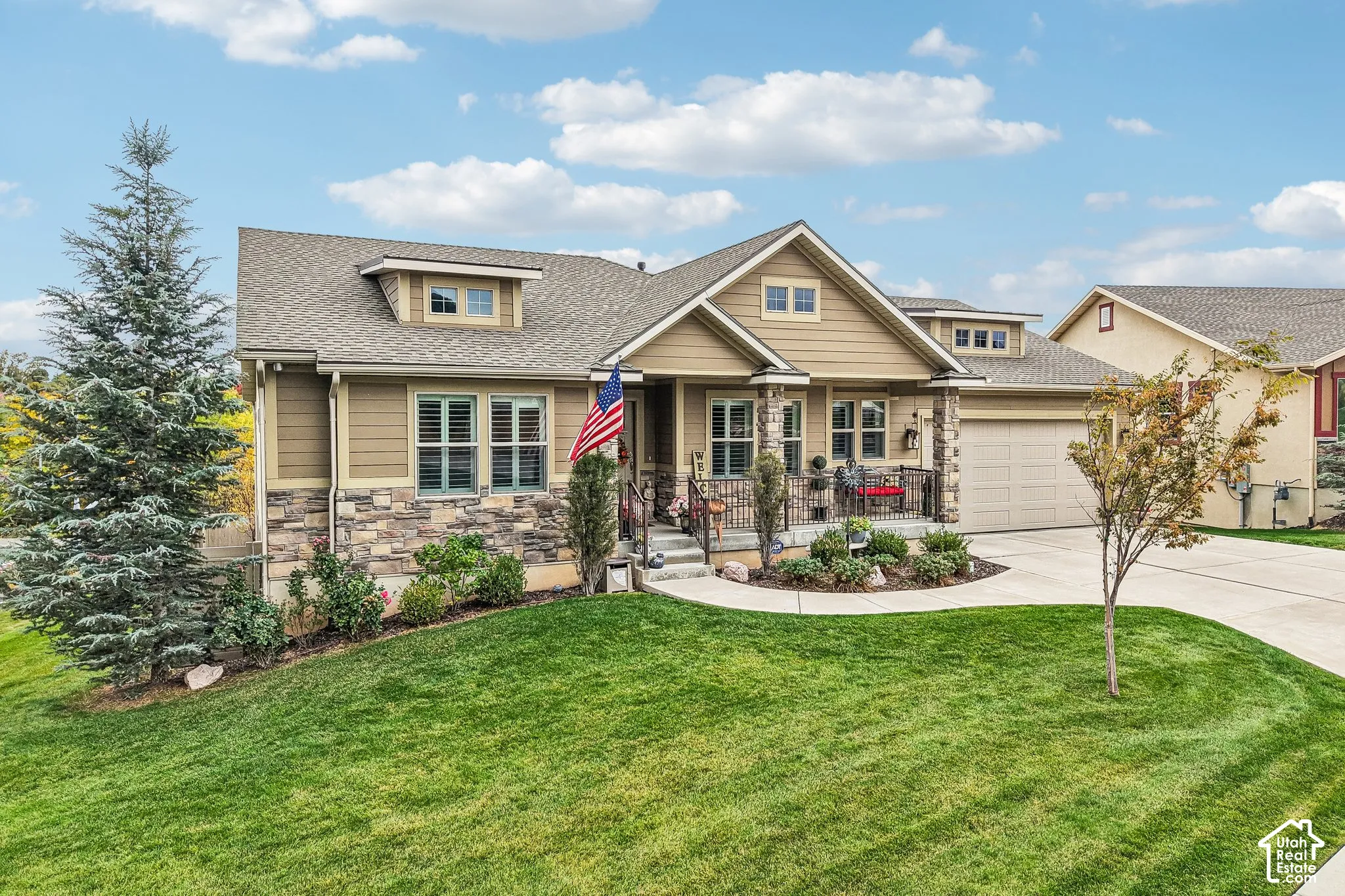 Exterior facade featuring horizontal siding and stacked stone masonry, gabled rooflines, a covered front porch with iron railing, and an attached garage
