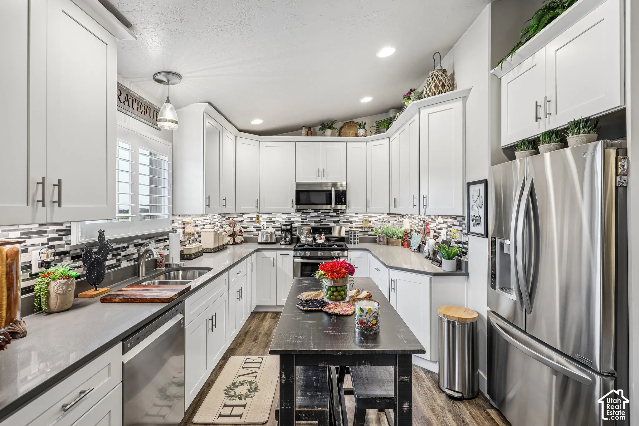 Kitchen featuring white shaker-style cabinetry, stainless steel appliances, quartz countertops, a multi-tonal linear tile backsplash, and wood-finish flooring