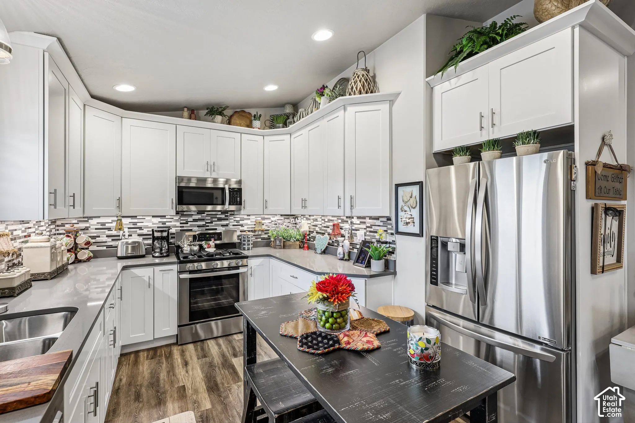 Kitchen featuring white shaker-style cabinetry, stainless steel appliances, quartz countertops, a multi-tone tile backsplash, and wood-finish flooring