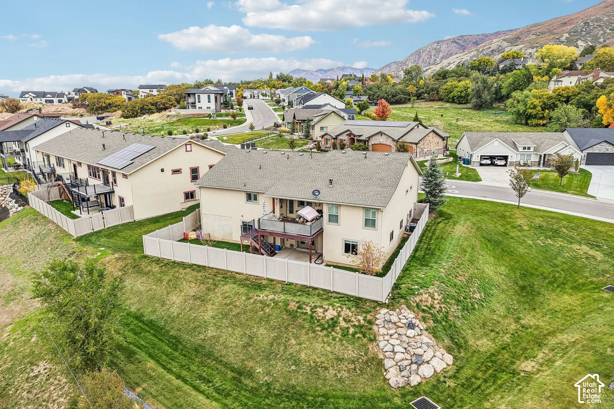 Two-story residence featuring an elevated rear deck, fenced backyard, exterior solar panels, and mountain backdrop
