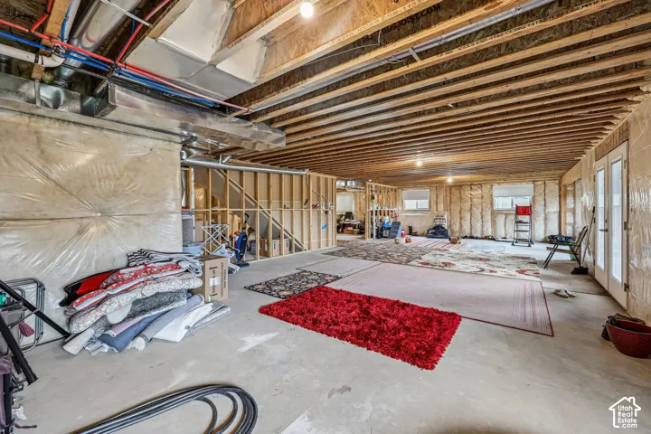 Unfinished basement featuring exposed wood joist ceilings, concrete flooring, perimeter framing, and double-door exterior access