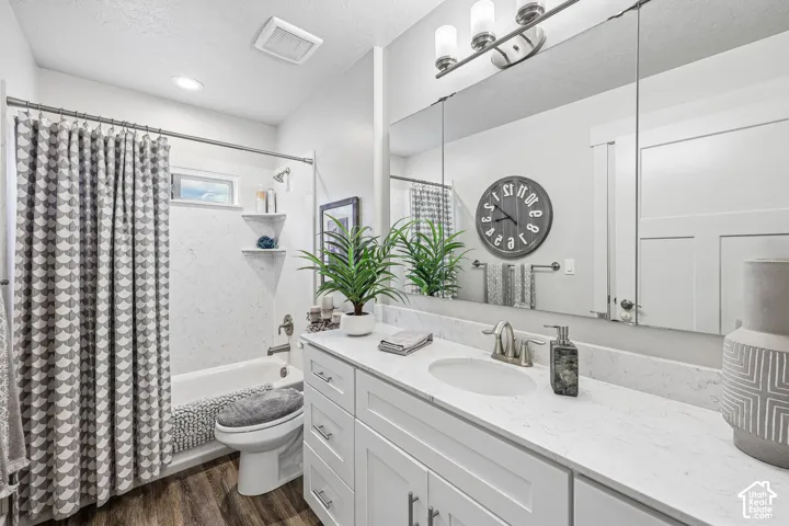 Bathroom featuring a white vanity with a stone-composite countertop, integrated sink, large wall-spanning mirror, wood-finish flooring, and a tub-shower combination with built-in corner shelving