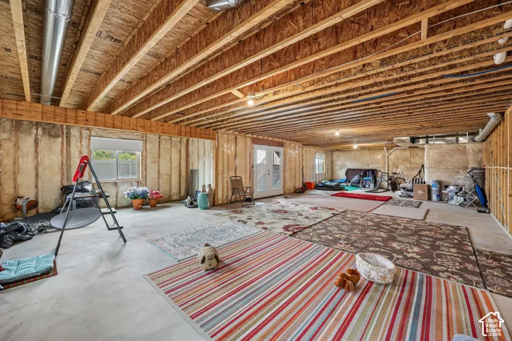 Unfinished lower level featuring exposed wood-joist ceilings, concrete flooring, insulated wall panels, and direct-access double doors