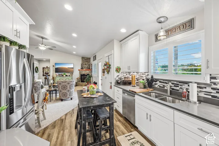 Kitchen featuring white cabinetry, solid surface countertops, stainless steel appliances, a multi-tonal tile backsplash, and wood-finish flooring