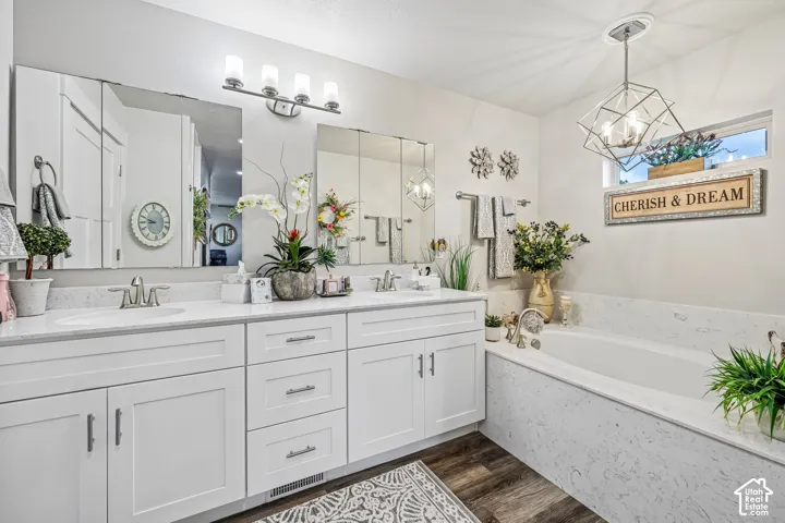 Double vanity with white cabinetry, stone-surfaced countertops, recessed medicine cabinets, and geometric pendant lighting, complemented by a built-in soaking tub with matching stone surround and wood-finish flooring