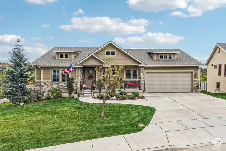 Craftsman-style residence featuring horizontal siding, decorative stone masonry accents, a covered front porch, dual front-facing gabled dormers, and an attached two-car garage