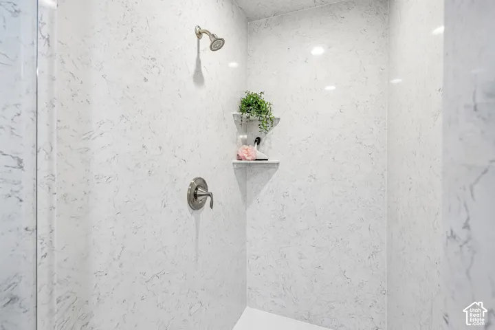 Shower enclosure featuring full-height stone-patterned wall panels, brushed-nickel single-handle pressure balance valve, fixed shower head, and dual built-in corner shelves