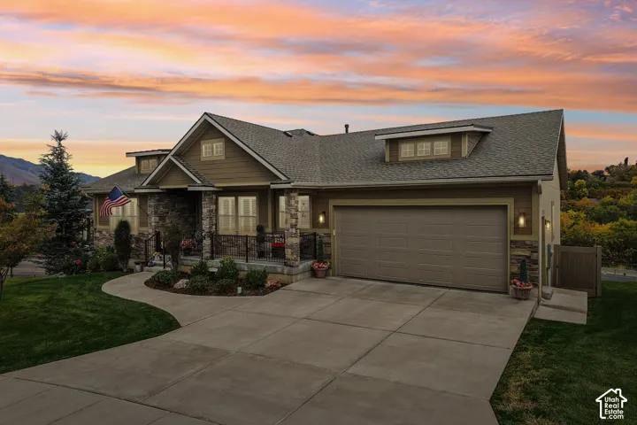 Exterior featuring horizontal siding with stone veneer accents, multi-gabled roofline, concrete driveway, and covered porch with metal railing