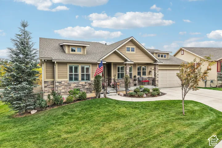 Exterior facade featuring horizontal siding and stacked stone masonry, gabled rooflines, a covered front porch with iron railing, and an attached garage