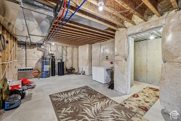 Unfinished basement featuring exposed floor joists, concrete foundation walls with vapor barrier insulation, metal ductwork, and water heating system