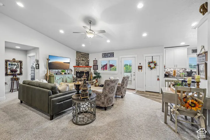 Open concept interior featuring vaulted ceilings, recessed lighting, a stone-accented fireplace with a wood mantel, and wood-finish flooring