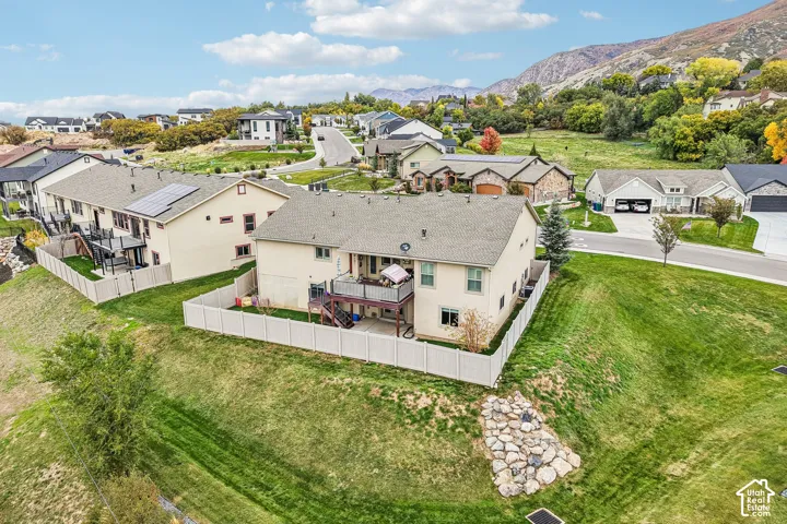 Two-story residence featuring an elevated rear deck, fenced backyard, exterior solar panels, and mountain backdrop