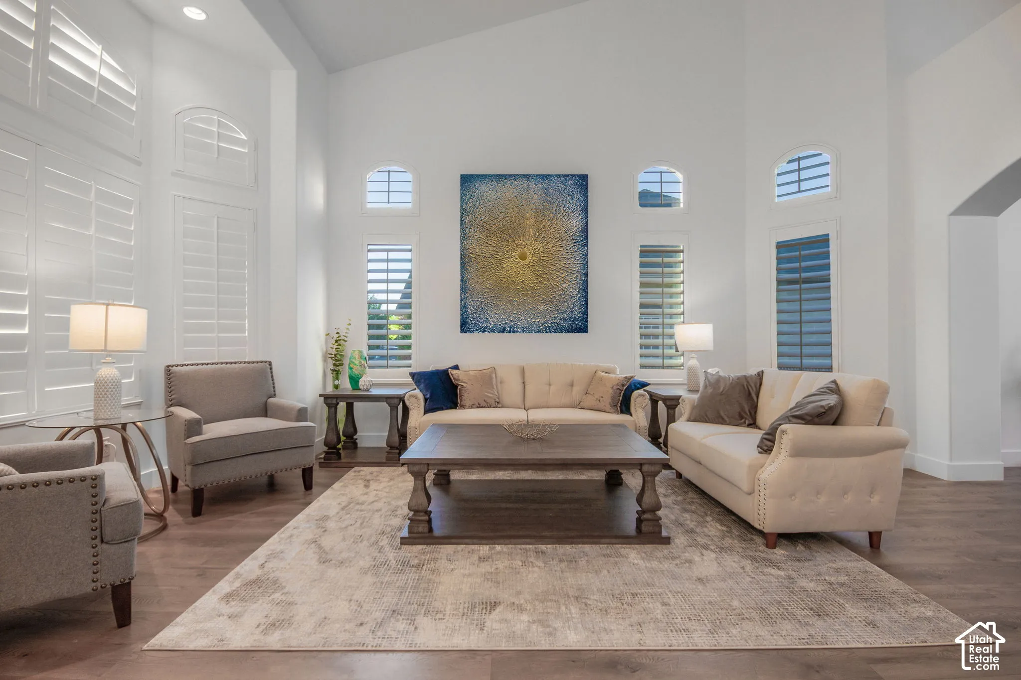 Vaulted ceilings, wood-finish flooring, and multiple arched windows featuring plantation shutters