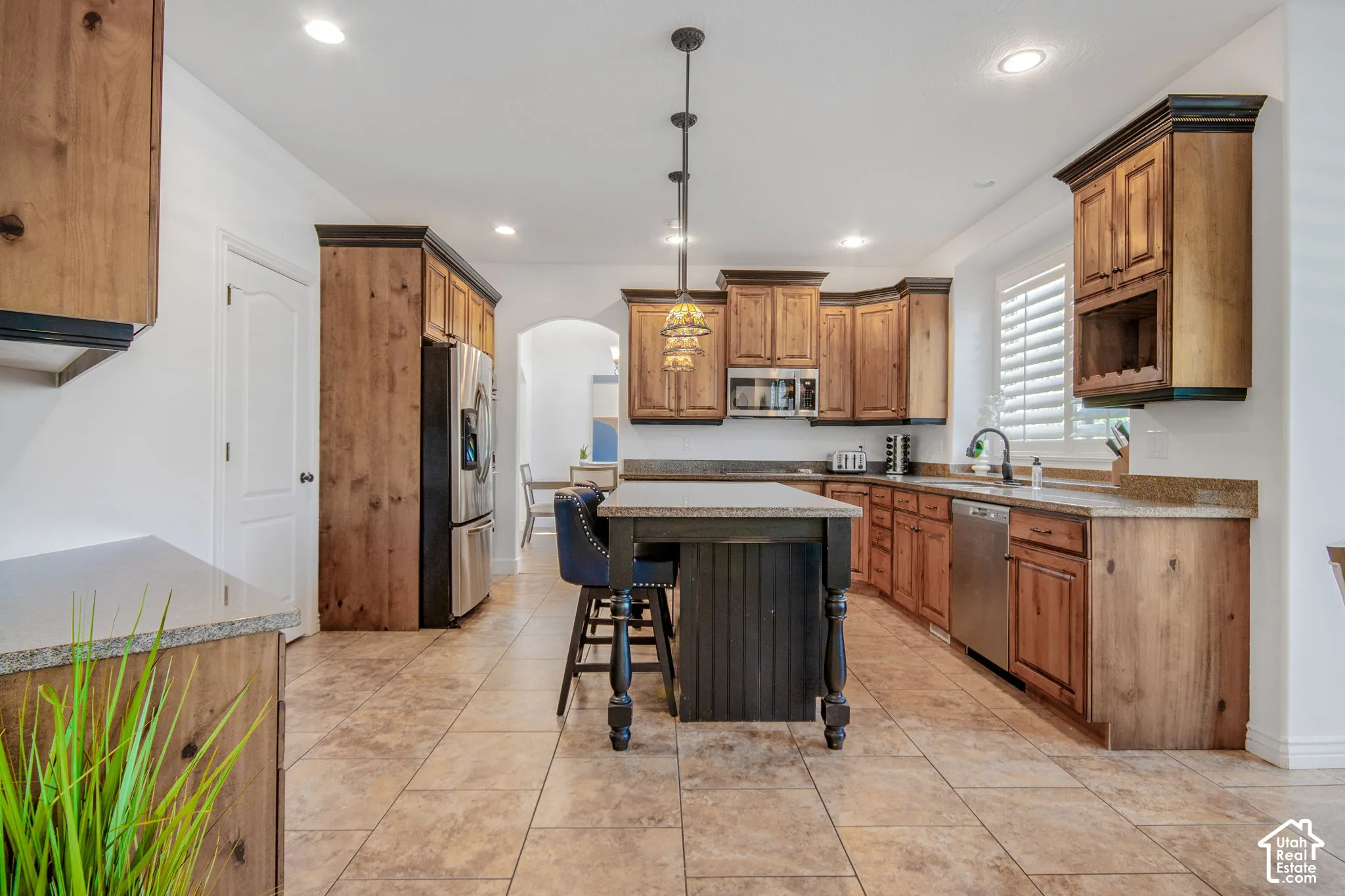 Kitchen featuring stained wood cabinetry, stone-finish countertops, tile flooring, stainless steel appliances, and a center island with pendant lighting
