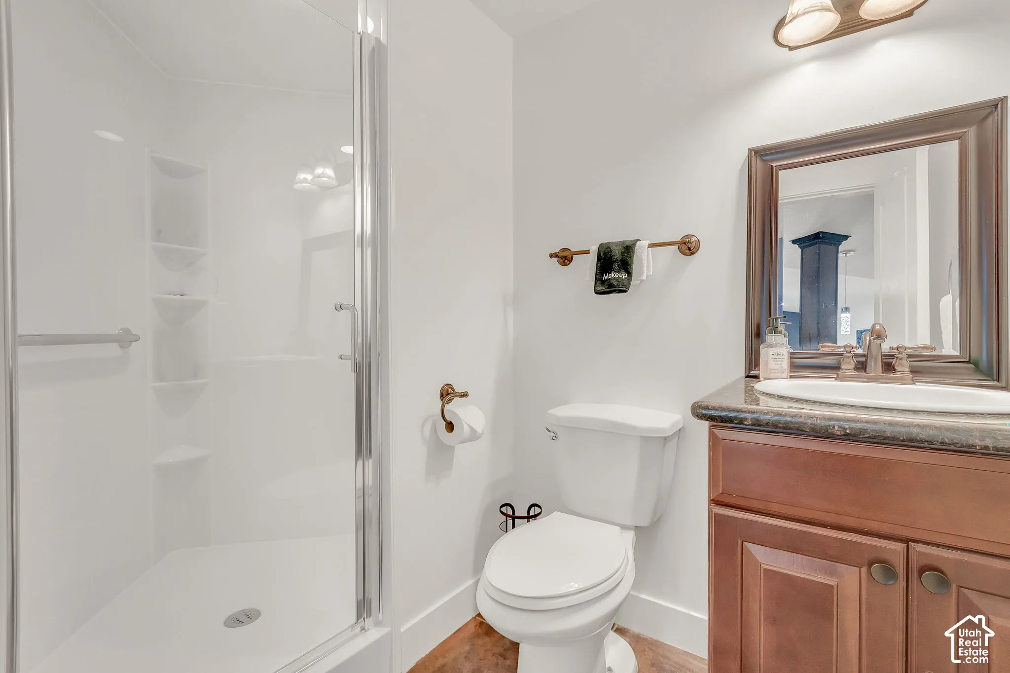 Bathroom featuring a shower stall with a glass door and built-in shelving, dark-toned cabinetry, an integrated vanity top with an undermount sink, and bronze-finished hardware