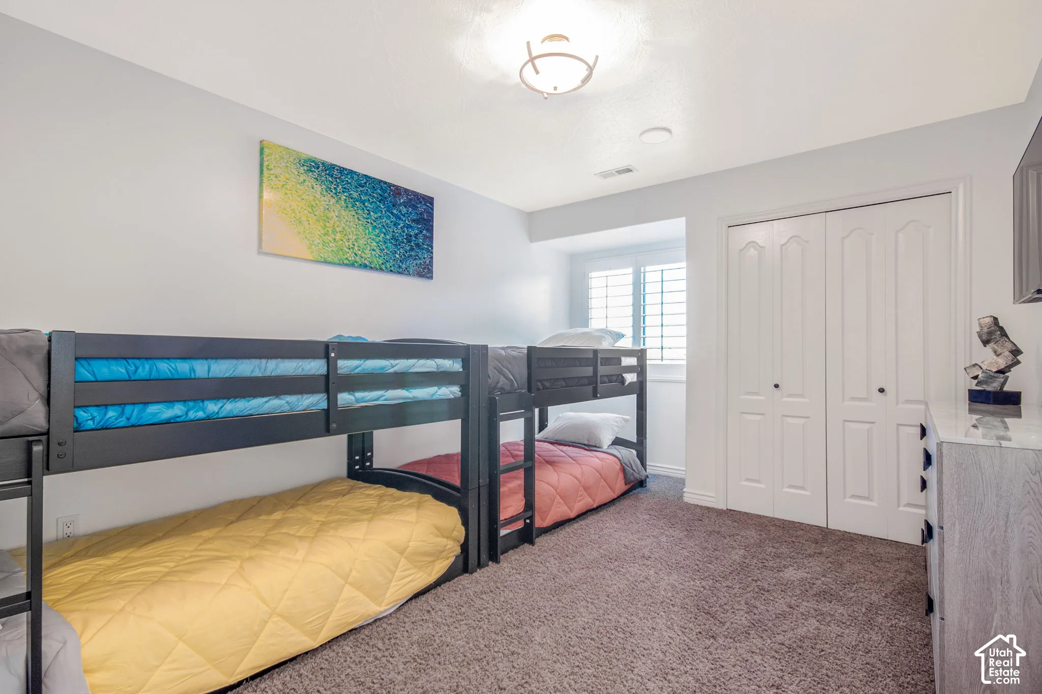 Room with neutral carpeting, double-door closet with raised-panel detailing, window featuring interior plantation shutters, and ceiling-mounted light fixture