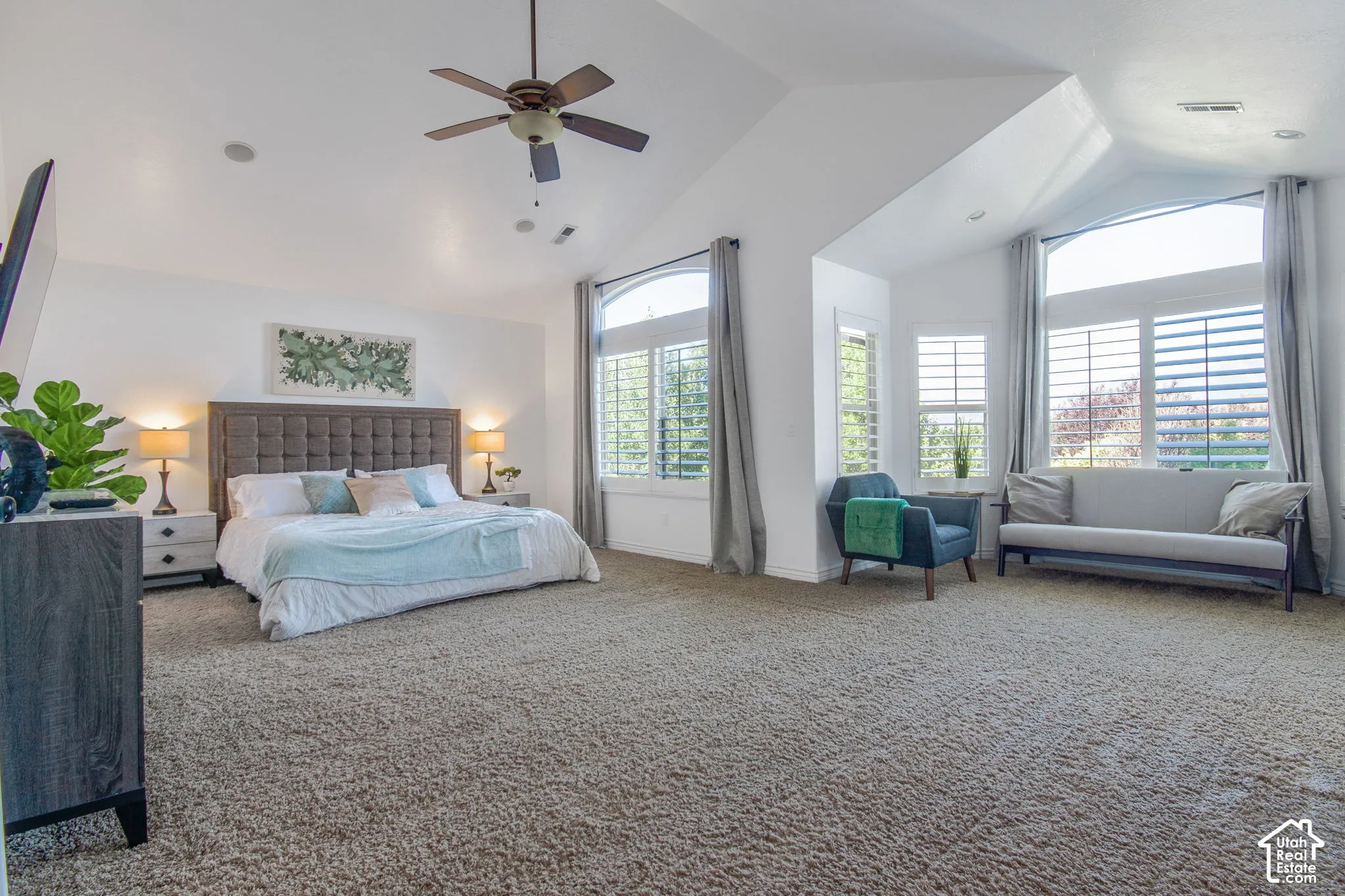 Vaulted ceilings, expansive windows with arch-top detailing, plantation shutters, and a ceiling fan