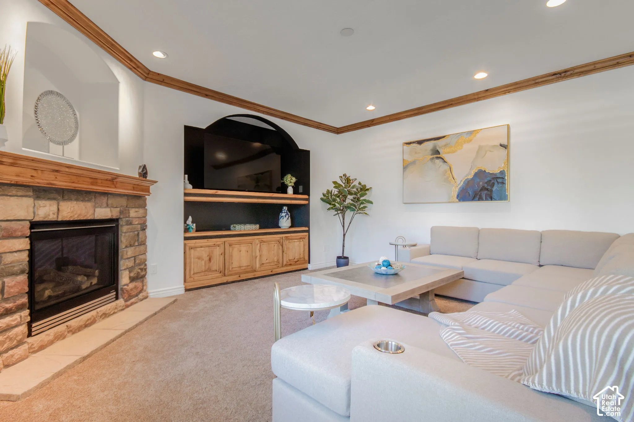 Stone-clad fireplace with a wood mantel, arched architectural wall niche, custom built-in cabinetry, crown molding, and recessed lighting