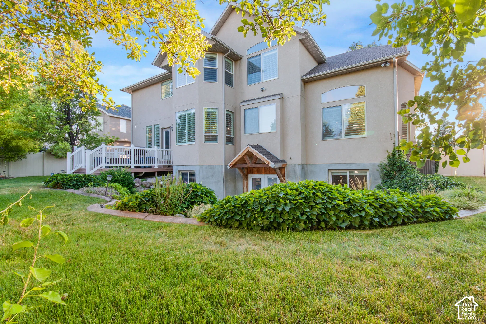 Multi-level residence featuring stucco siding, multi-pane windows with arched detailing, a raised deck with white railing, and a covered ground-level entryway